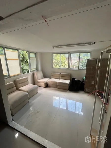 店屋 出租在Khlong Toei, Bangkok - 明亮休闲室，白色地砖、模块沙发与大窗，外望绿意。