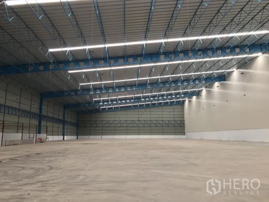 Warehouse for rent in Samut Prakan - Column-free warehouse span with blue steel beams, insulated roof panels, and a large open floor area.
