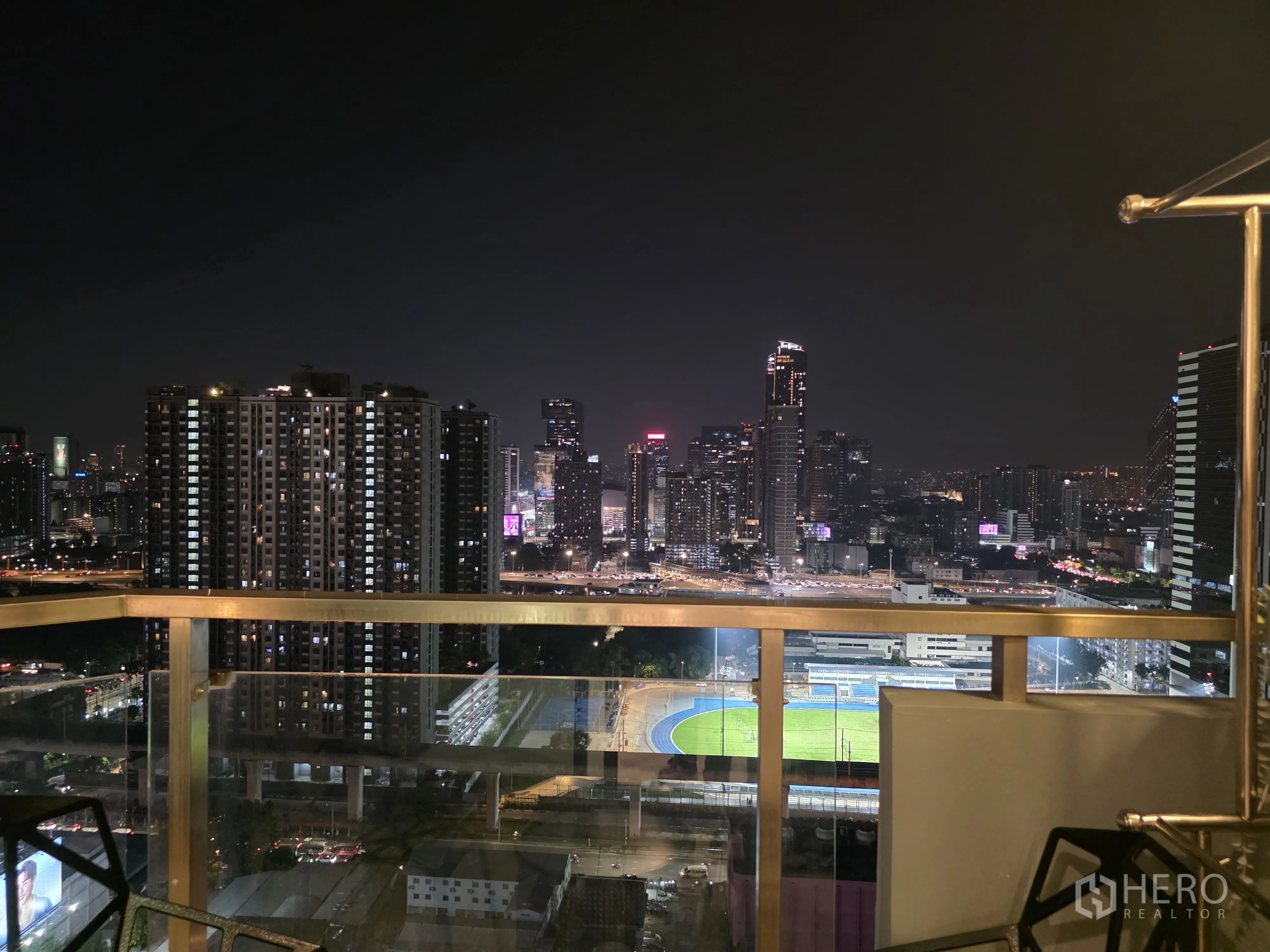 Condominium for rent in Bang Kapi, Bangkok - High-floor balcony view of the city skyline and illuminated sports field at night.