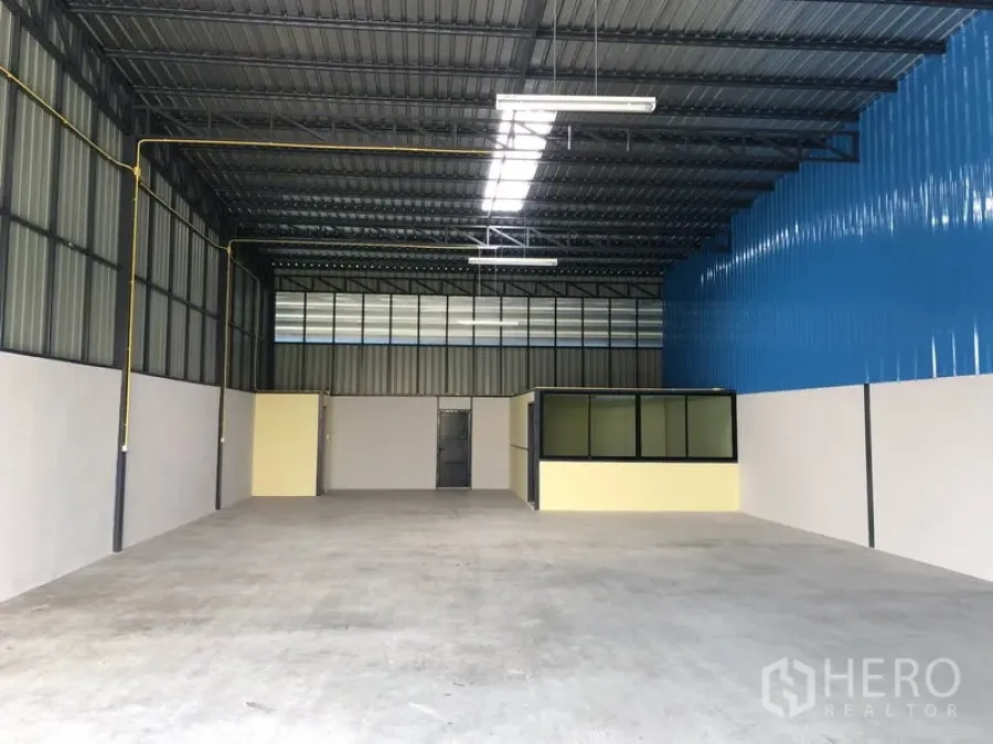 货栈 出租在Khlong Luang, Pathum Thani - 仓库内部，高钢结构屋顶带采光带，平整混凝土地面与小型玻璃隔断办公室。