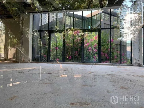 Office Space for rent in Khlong Toei, Bangkok - Bright empty office with floor-to-ceiling glass looking onto a lush garden with pink flowers.