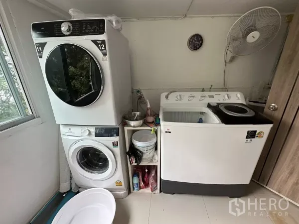 Retail Space for rent - Compact laundry area with stacked washer and dryer next to a top-load machine by a window.