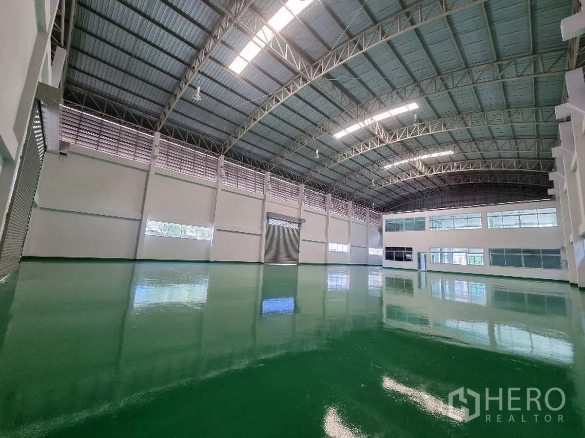 Factory for rent in Samut Prakan - Open warehouse interior with skylights, multiple roller shutters and internal office windows.