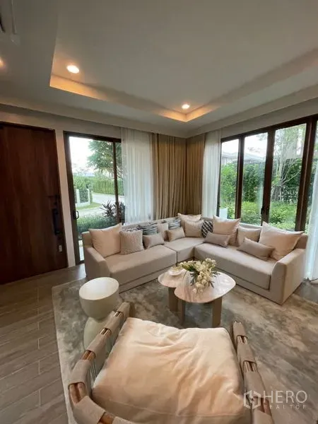 Detached House for sale in Bang Kapi, Bangkok - Bright living room with an L-shaped sofa, floor-to-ceiling windows, sheer curtains and recessed ceiling lights.