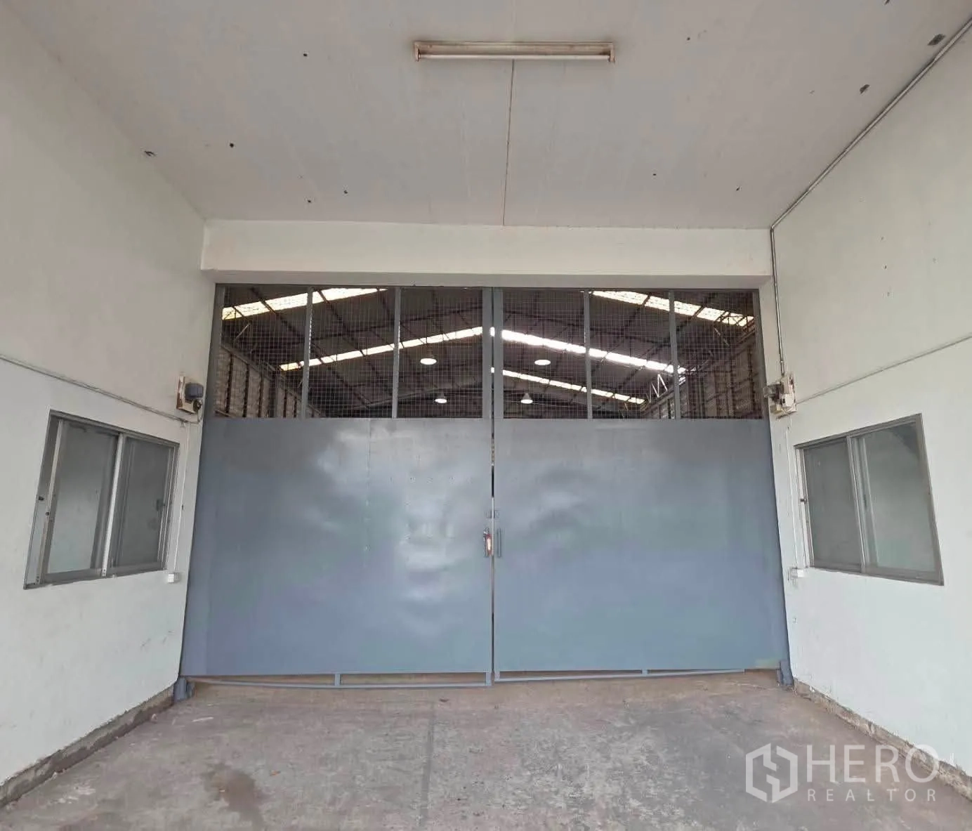 Warehouse for rent or sale in Phra Khanong, Bangkok - Wide metal double doors leading into the warehouse with windows on both sides.