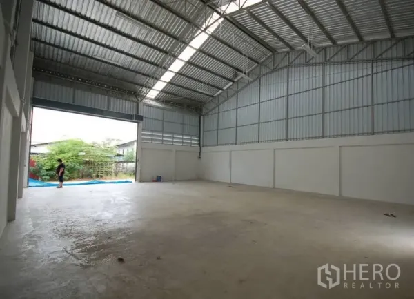 货栈 出租在Nonthaburi - 高挑金属屋顶的仓库内部，天窗采光，宽大卷闸门通向外部。