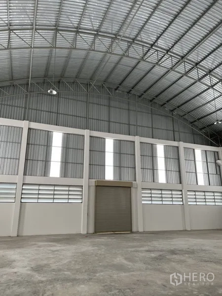 Factory for rent or sale in Bang Bo, Samut Prakan - Warehouse wall with translucent panels and a central roller door under a high roof.