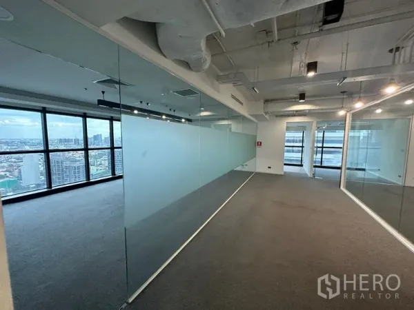 Office Space for rent - Open-plan Bangkok office with glass partition wall, carpet flooring, exposed ceiling and city skyline views.