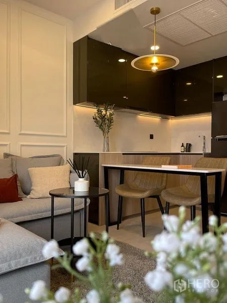 Condominium for rent in Pathum Wan, Bangkok - Open-plan living and kitchen with sofa, brass pendant light and breakfast bar.