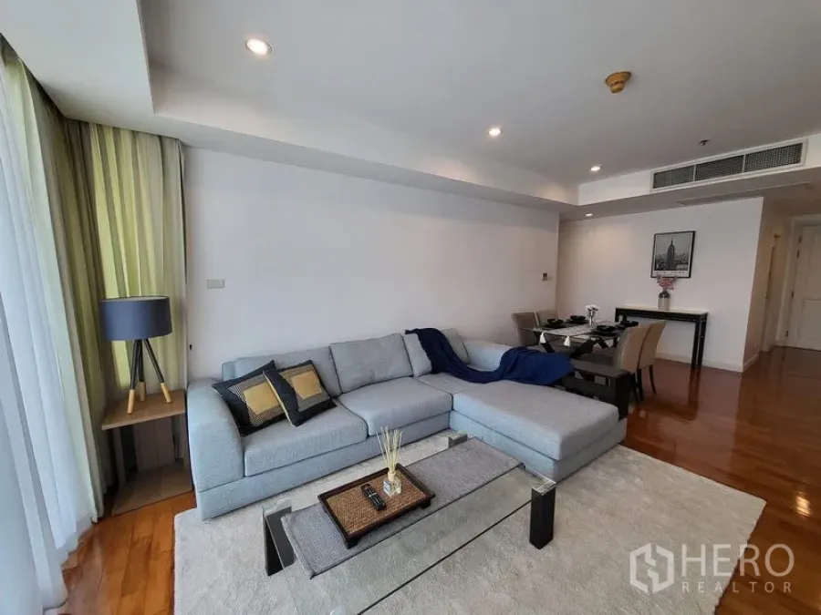 Condominium for rent in Khlong Toei, Bangkok - Spacious lounge with L-shaped sofa, recessed lighting and large rug beside the dining table.