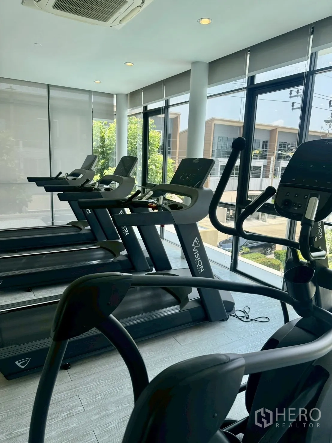 Townhouse for rent in Prawet, Bangkok - Fitness room with treadmills and elliptical machines by large windows.