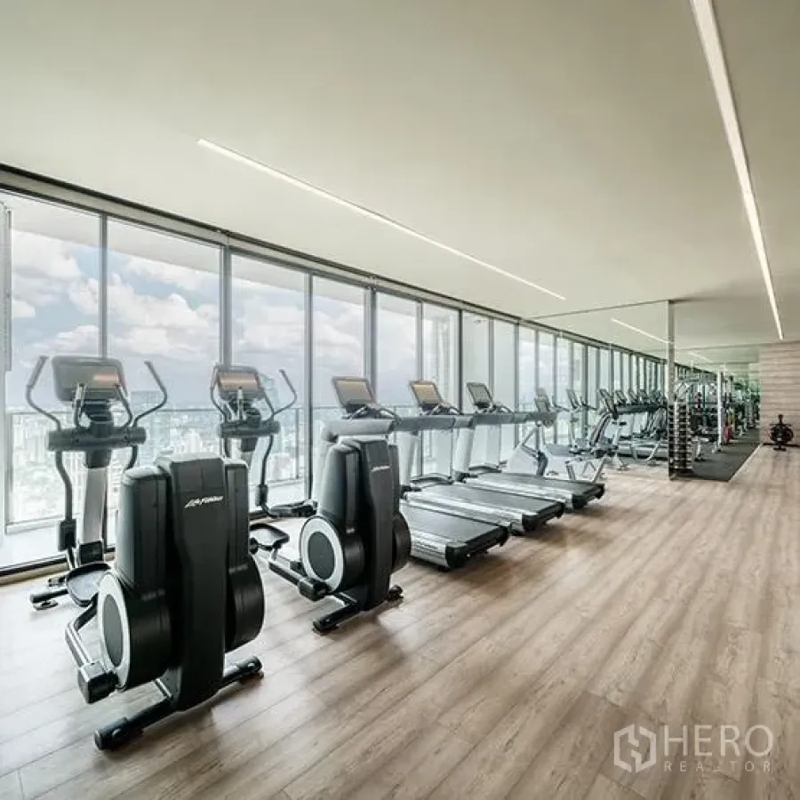 Condominium for rent or sale in Khlong Toei, Bangkok - Condominium fitness room with treadmills and bikes facing full-height windows and city views.