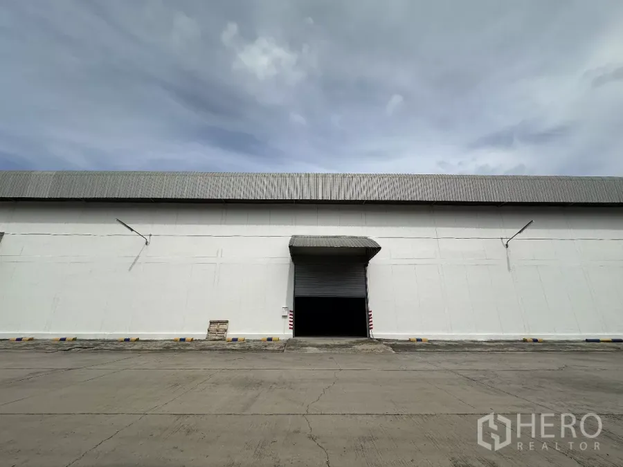 Warehouse for rent in Phra Nakhon Si Ayutthaya - Large warehouse facade with roller shutter loading bay and wide concrete apron under an overcast sky in Wang Noi.