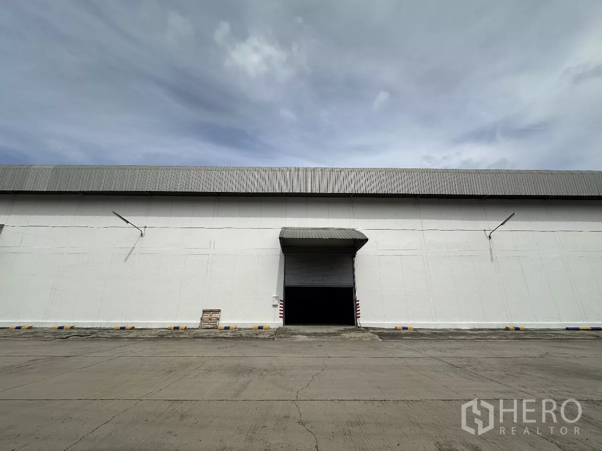 Warehouse for rent in Phra Nakhon Si Ayutthaya - Large warehouse facade with roller shutter loading bay and wide concrete apron under an overcast sky in Wang Noi.