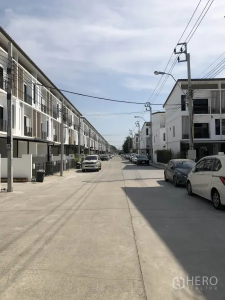 Townhouse for rent in Bang Kapi, Bangkok - Wide internal street lined with new three-storey townhomes and parked cars in a quiet gated community.