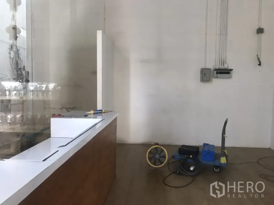 Retail Space for rent in Khlong Toei, Bangkok - Compact retail unit interior with white walls, wood-look flooring, a white service counter, electrical panels and a small equipment cart.