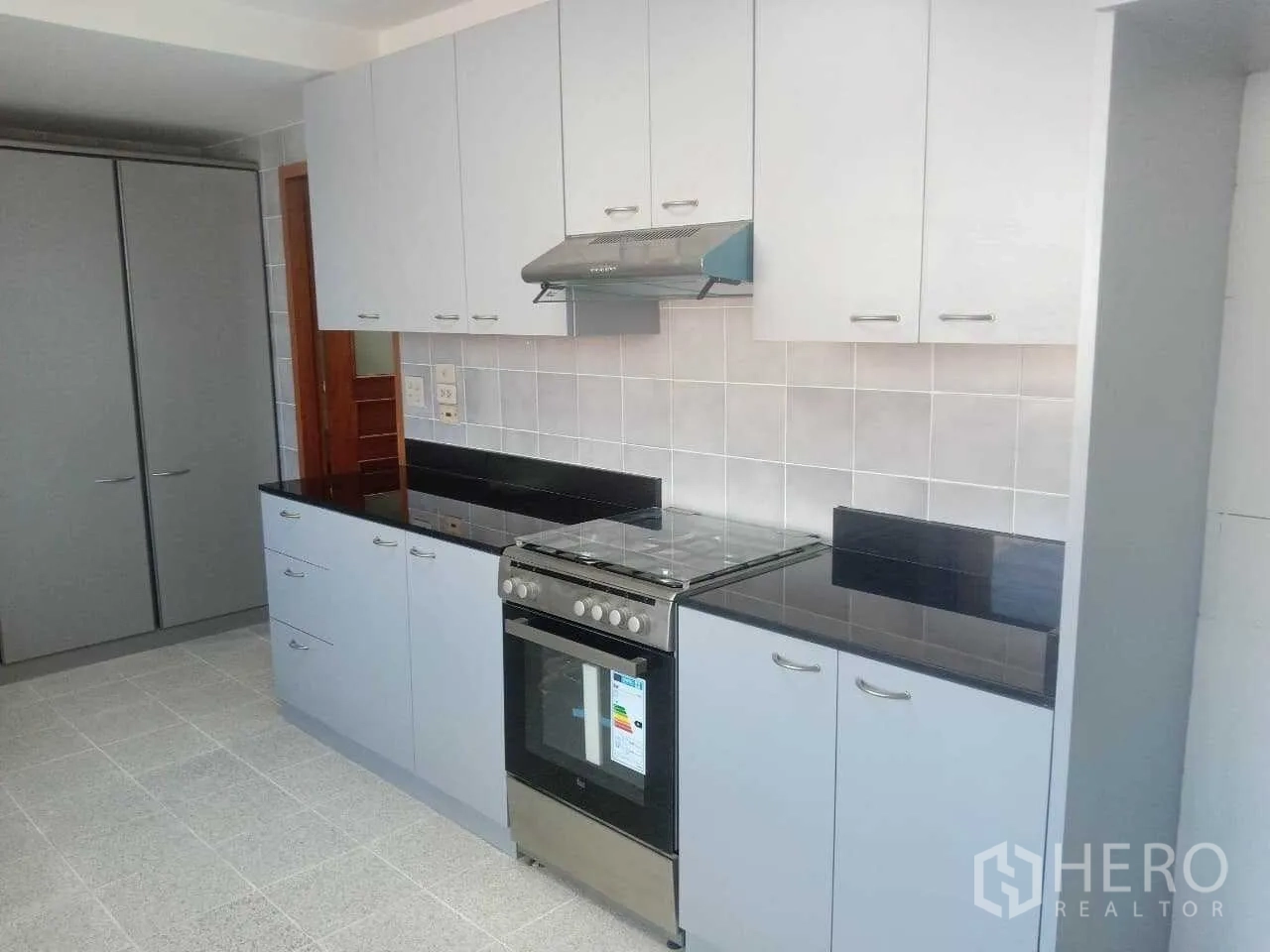 Condominium for rent in Khlong Toei, Bangkok - Modern kitchen with white cabinetry, black granite countertops and gas stove with oven.