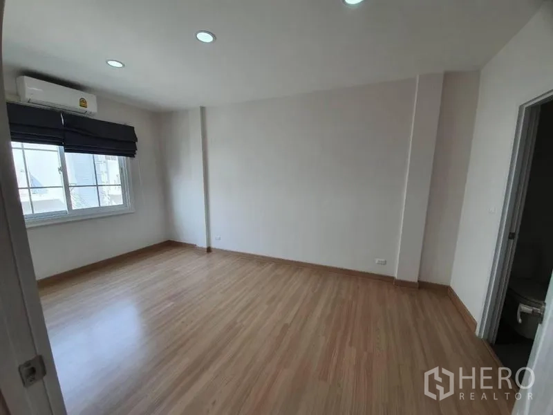 Townhouse for rent in Bang Na, Bangkok - Spacious bedroom with wood laminate floors, window blinds, air conditioner and ensuite access.