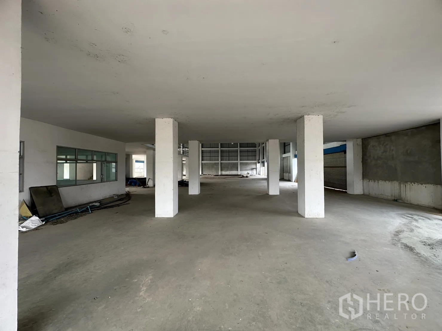 Factory for rent in Pak Kret, Nonthaburi - Covered loading and staging area beneath mezzanine with concrete floor and roller shutter.