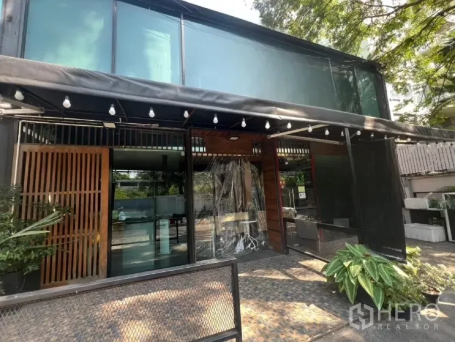 Retail Space for rent in Watthana, Bangkok - Glass-fronted two-storey retail unit with canopy lights, patio seating area, and greenery at the entrance.