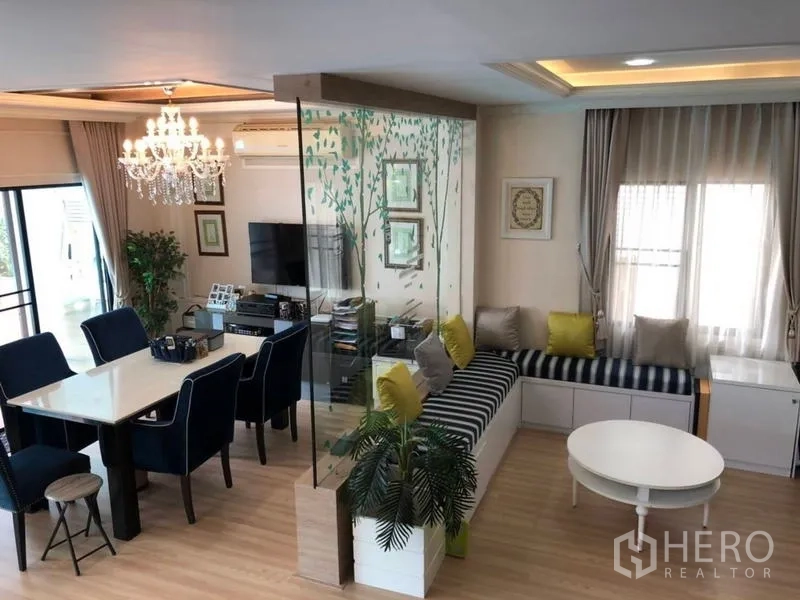 Detached House for sale in Lam Luk Ka, Pathum Thani - Bright open-plan dining and living area with chandelier, glass divider and built-in bench seating.