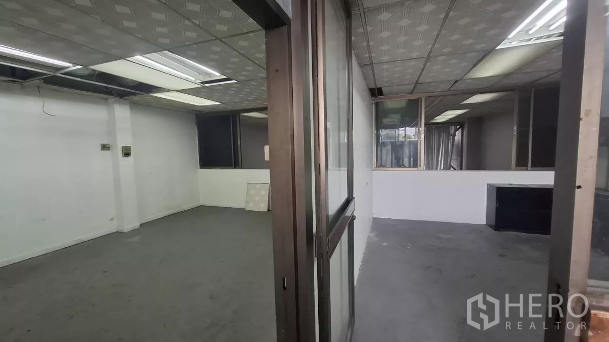 Shophouse for rent in Watthana, Bangkok - Two adjoining rooms with sliding glass doors and drop-ceiling lighting.