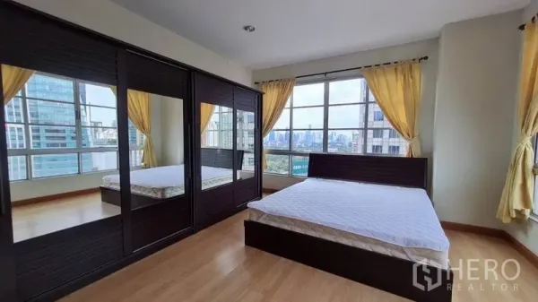 Condominium for rent in Khlong Toei, Bangkok - Primary bedroom with mirrored wardrobes, wood floors and wide windows with city views.