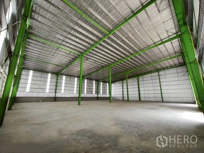 Warehouse for rent in Bang Phli, Samut Prakan - Spacious warehouse interior with high roof, green steel columns, and smooth concrete floor.