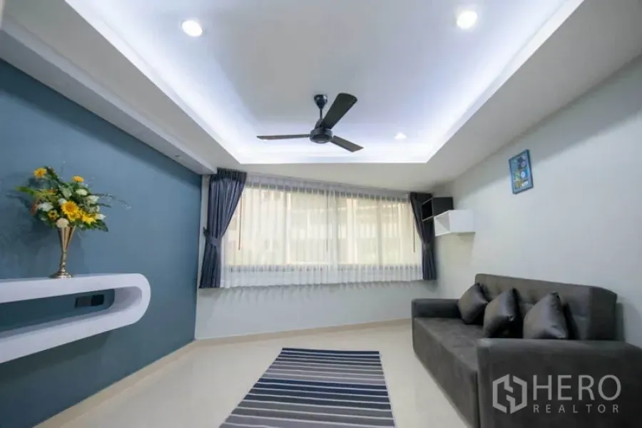 Condominium for rent in Khlong Toei, Bangkok - Bright living room with tray ceiling, ceiling fan, blue accent wall, grey sofa and striped rug.