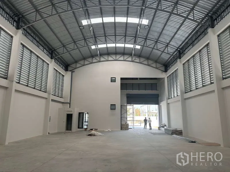 Factory for sale in Lam Luk Ka, Pathum Thani - Spacious high-clearance warehouse interior with steel truss roof, ventilated louver panels and wide roller door.