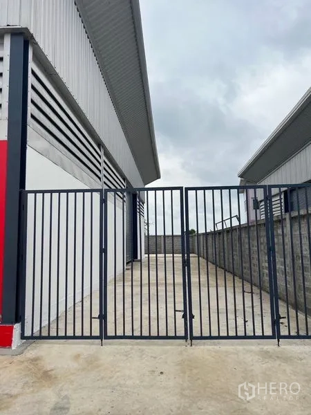 Warehouse for rent or sale in Sai Noi, Nonthaburi - Black steel security gate opening to a concrete loading bay beside the warehouse.