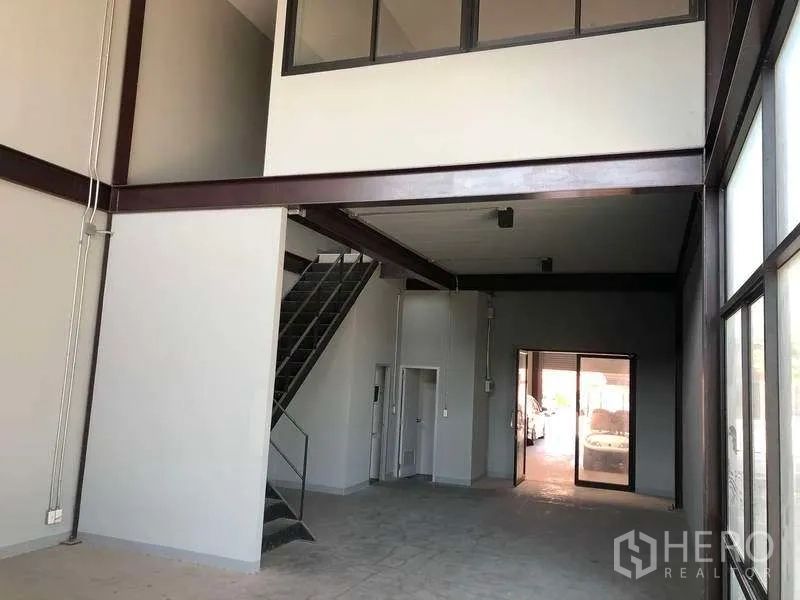Warehouse for rent in Bang Phli, Samut Prakan - Open hall with metal staircase leading to a glass-fronted mezzanine office and side windows.