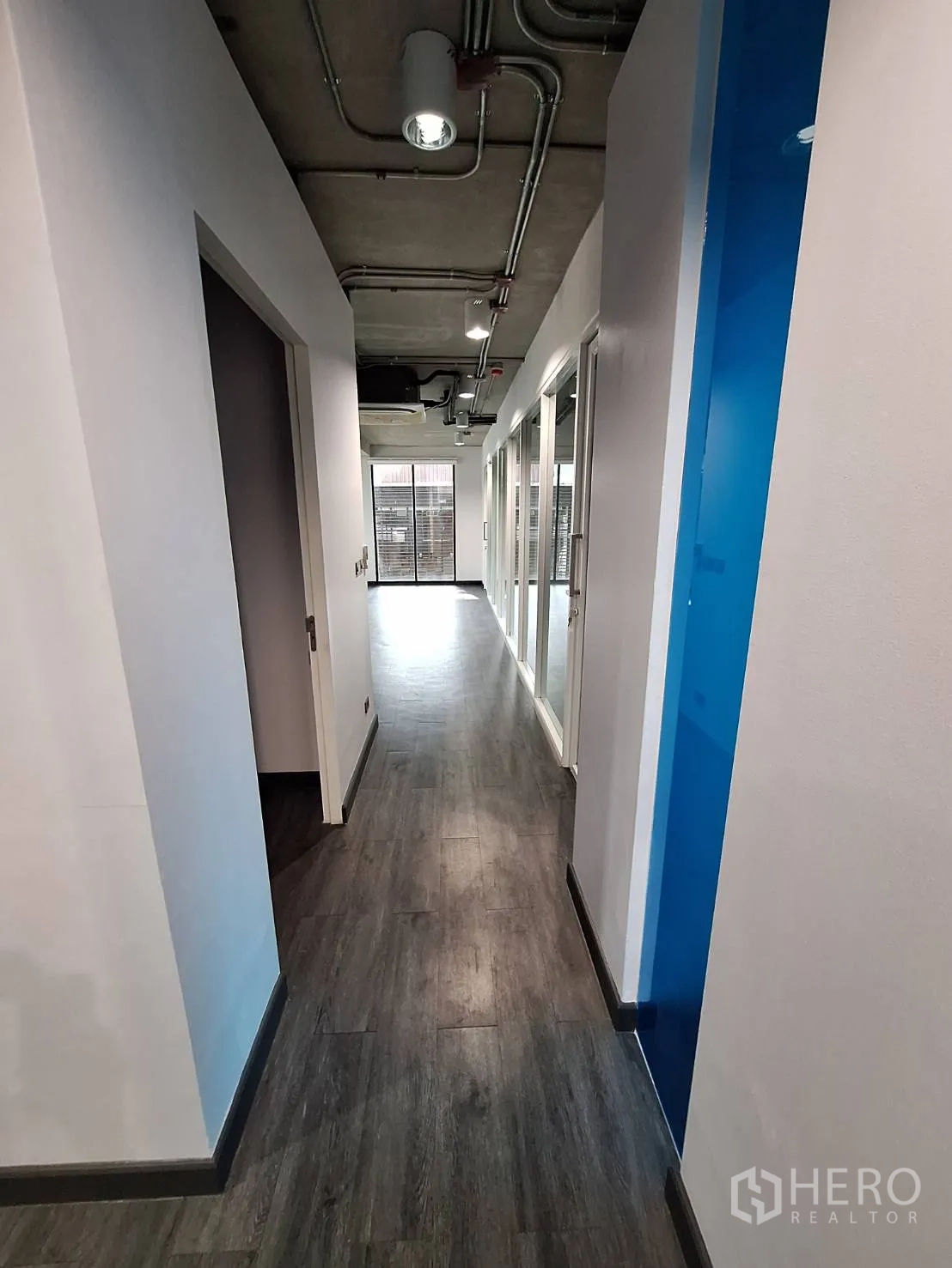 Office Space for rent - Thonglor office corridor with dark wood floors, exposed ceiling pipes and glass-partitioned rooms.