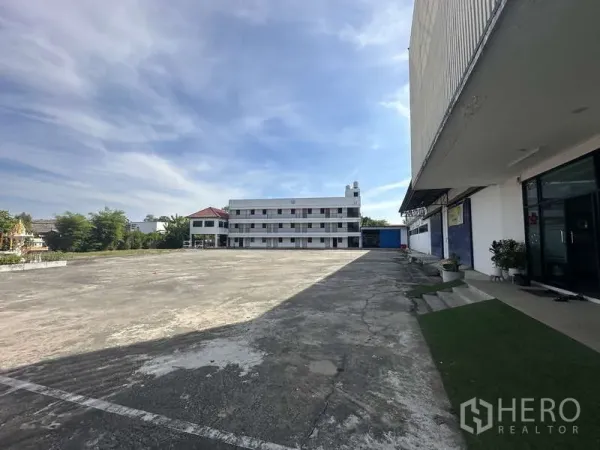 Warehouse for rent in Khlong Sam Wa, Bangkok - Wide concrete yard of an industrial complex with a multi‑storey building and clear sky.