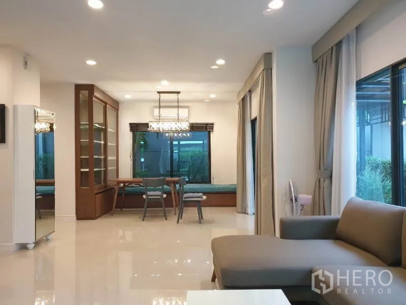 Detached House for rent in Bang Kapi, Bangkok - Bright open-plan living area with large windows, recessed lights, and a sectional sofa facing the dining zone.