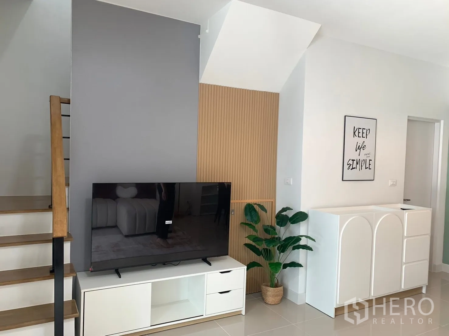 Townhouse for rent in Bang Phli, Samut Prakan - TV wall and staircase with minimalist cabinet, indoor plant and clean modern decor.