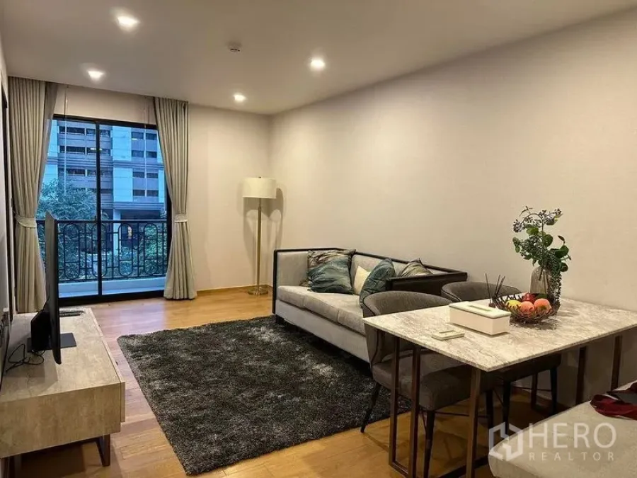 Condominium for rent in Pathum Wan, Bangkok - Living and dining area with sofa, TV console, rug, and sliding doors to a balcony.