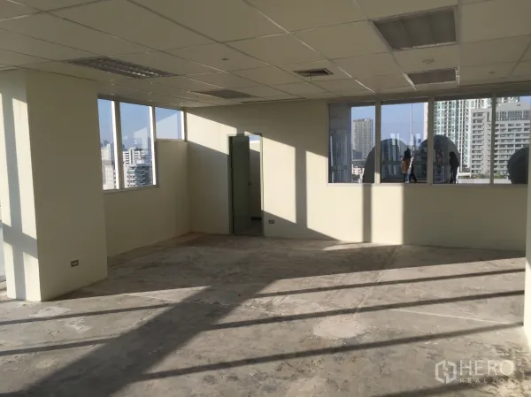 Office Space for rent in Khlong Toei, Bangkok - Bright open-plan office with grid ceiling and large windows on two sides, plus a door to private facilities.