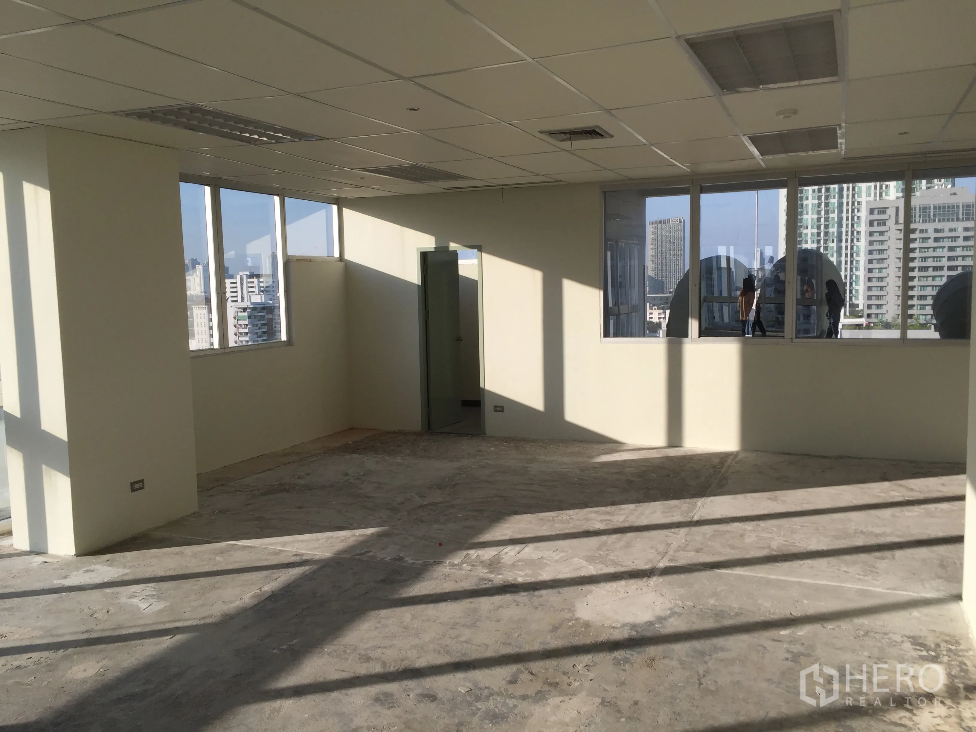 Office Space for rent in Khlong Toei, Bangkok - Bright open-plan office with grid ceiling and large windows on two sides, plus a door to private facilities.
