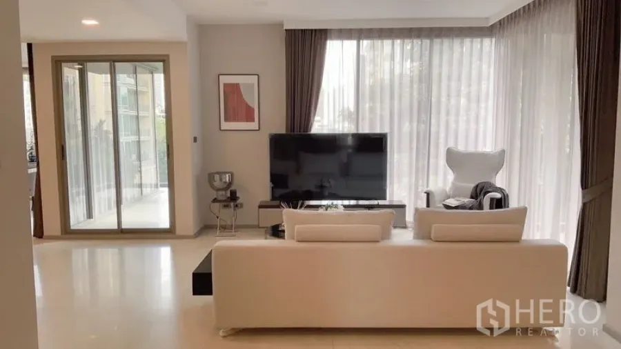 Condominium for rent in Watthana, Bangkok - Living room view to TV and balcony doors framed by sheer corner windows.