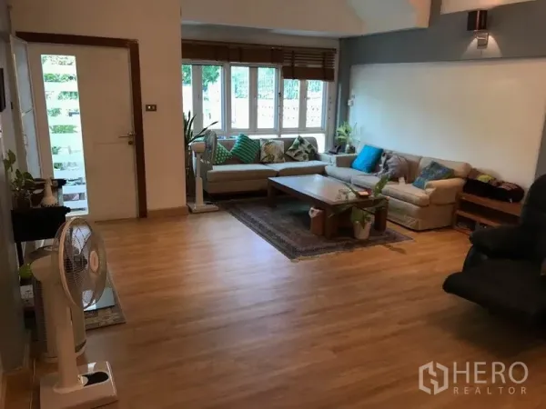 Townhouse for rent or sale in Khlong Toei, Bangkok - Bright living room with L-shaped sofa, large front windows and warm wood flooring.