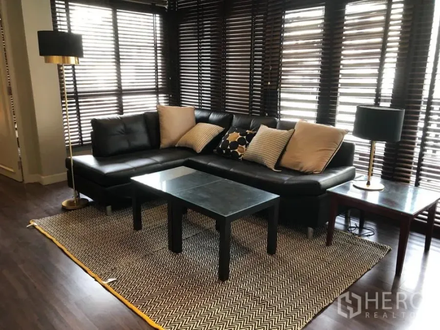 Condominium for rent in Khlong Toei, Bangkok - Bright living area with black leather sectional sofa, coffee table and chevron rug by full-height windows.