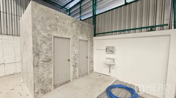 Warehouse for rent in Bang Bon, Bangkok - Warehouse interior with a concrete restroom block and wall-mounted sink under a metal roof.