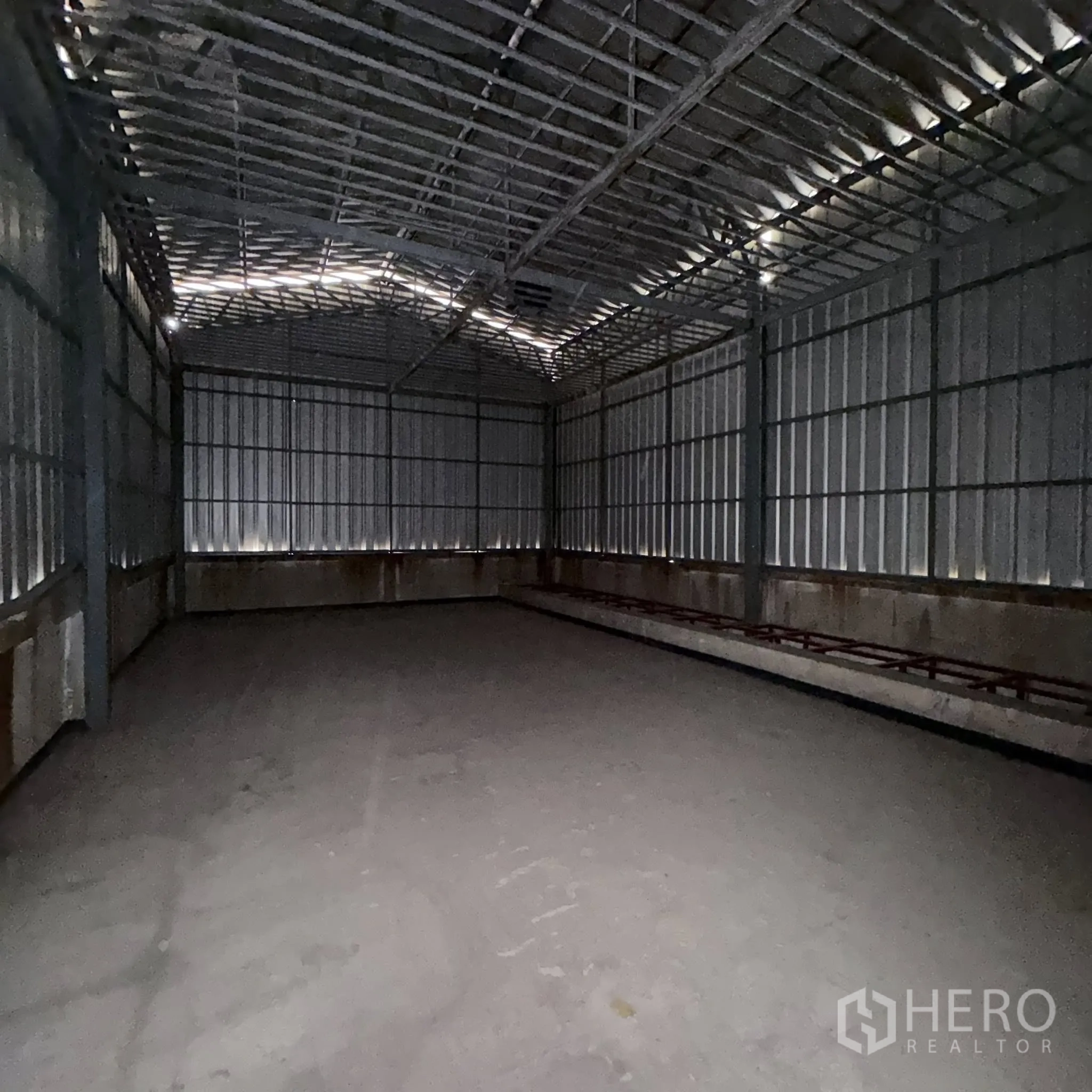 Factory for rent in Phra Pradaeng, Samut Prakan - Dim metal-clad storage hall with exposed roof trusses and solid floor.