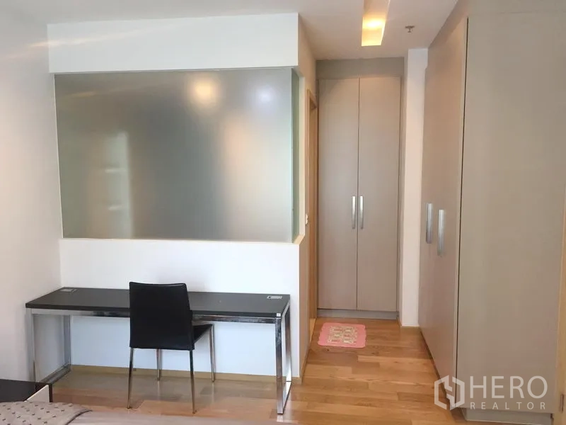Condominium for rent in Khlong Toei, Bangkok - Study nook with desk and chair beside built-in wardrobes and a frosted glass partition.