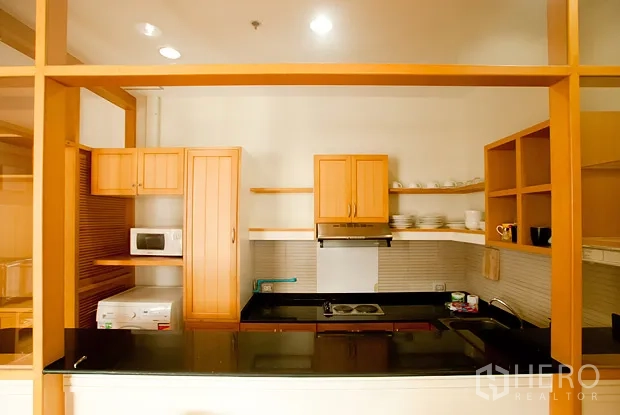 Condominium for rent in Khlong Toei, Bangkok - Open kitchen featuring wooden cabinetry, black granite countertop, cooktop and microwave.