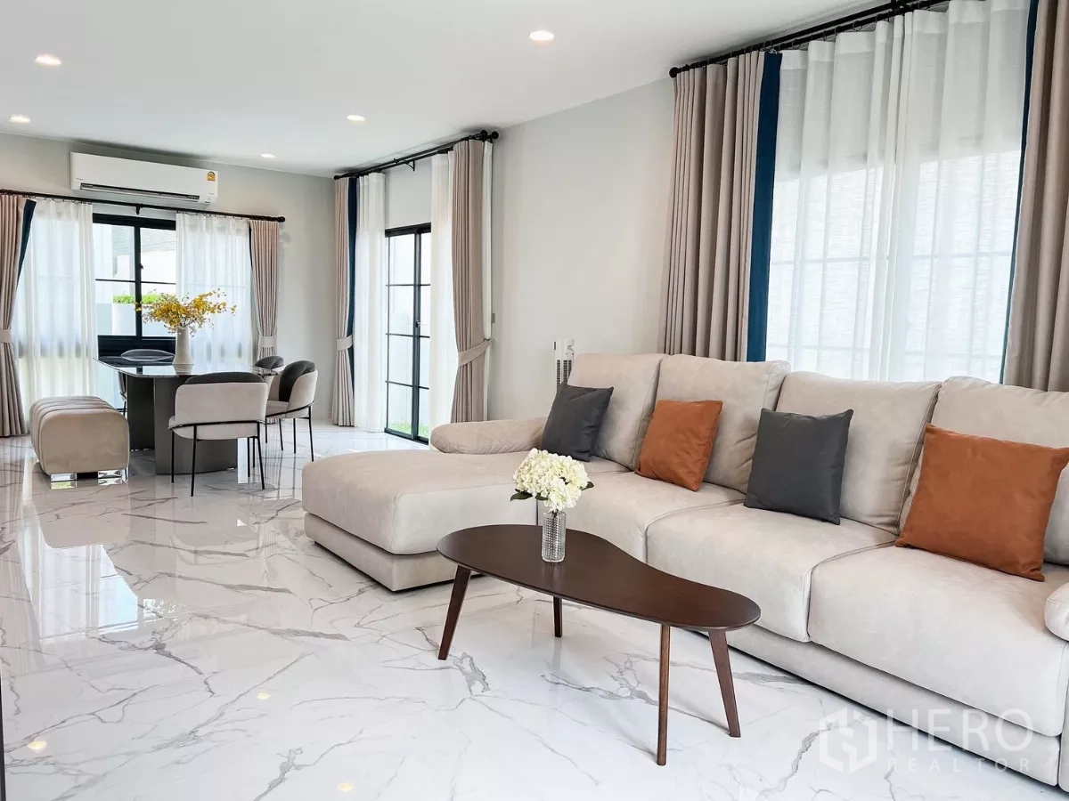 Detached House for rent in Khan Na Yao, Bangkok - Spacious lounge with L-shaped sofa, coffee table and sleek white marble flooring near the dining nook.