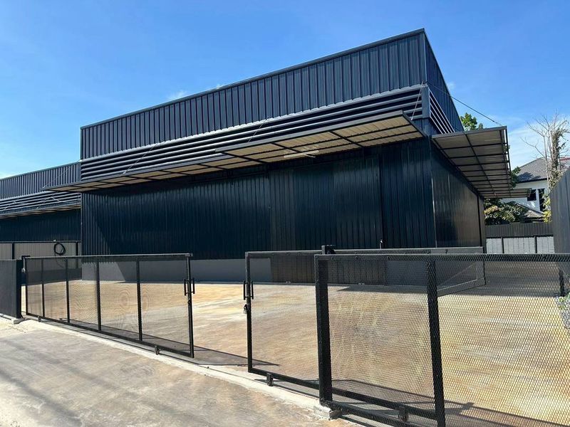 货栈 出租在Bueng Kum, Bangkok - 现代黑色金属外墙的仓库外观，车道宽阔，滑动金属网门及带遮雨装卸区。