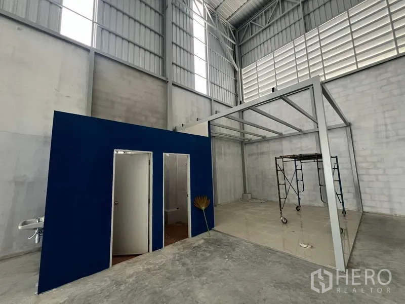 Warehouse for rent in Prawet, Bangkok - Warehouse interior with high ceiling, blue partitioned office and toilets, and a steel mezzanine frame.