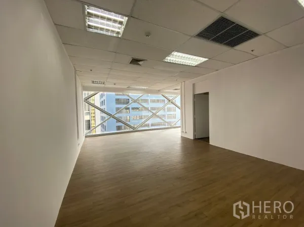 办公空间 出租在Watthana, Bangkok - 明亮的开放式办公室，木纹地板、格栅天花灯光与带X形立面的大窗，城市景观。